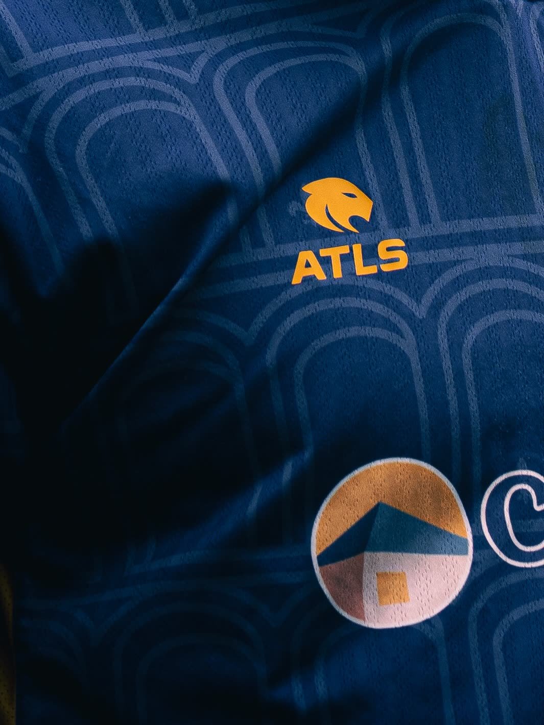 Détail du maillot : logo Atls brodé sur un tissu à motif d'arches